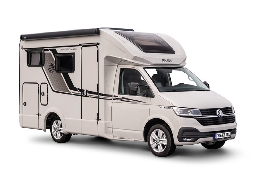 En Knaus Tourer Van Vansation 2024 autocamper, set fra siden. Billedet viser autocamperens moderne og kompakte design i hvid med sorte og grå detaljer. Køretøjet er udstyret med store vinduer og avancerede funktioner, hvilket gør den ideel til fleksible og komfortable rejser.